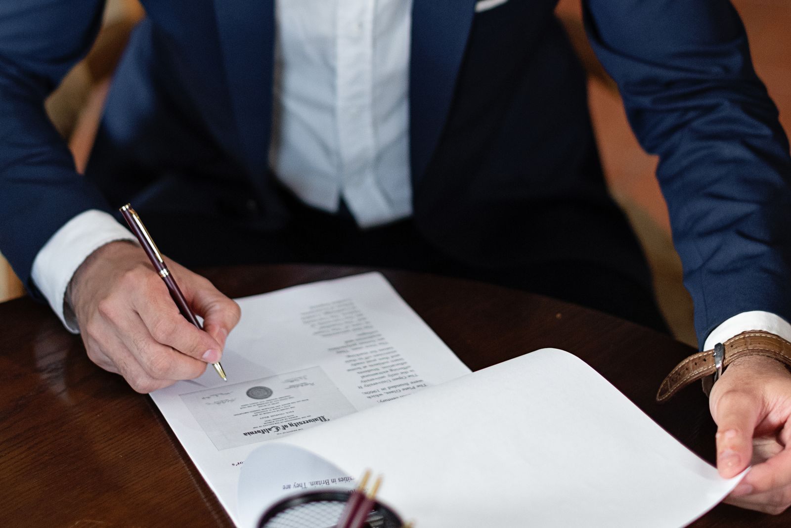 Man in a suit signing a document at a desk, like an agent signing a group cruise contract