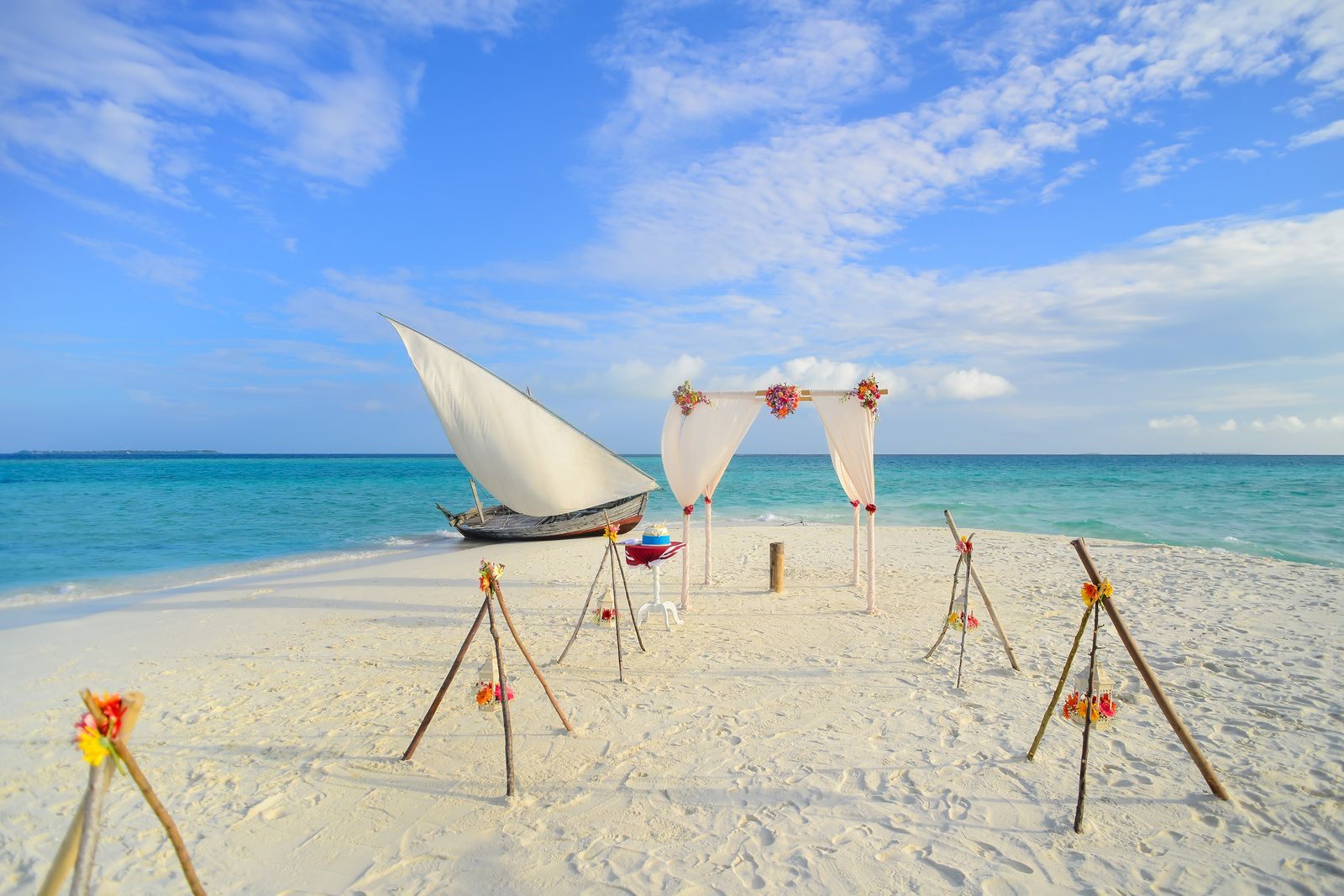 Beach set for a wedding ceremony with a sailboat moored in turquoise water, one of the celebrations behind cruise group sales