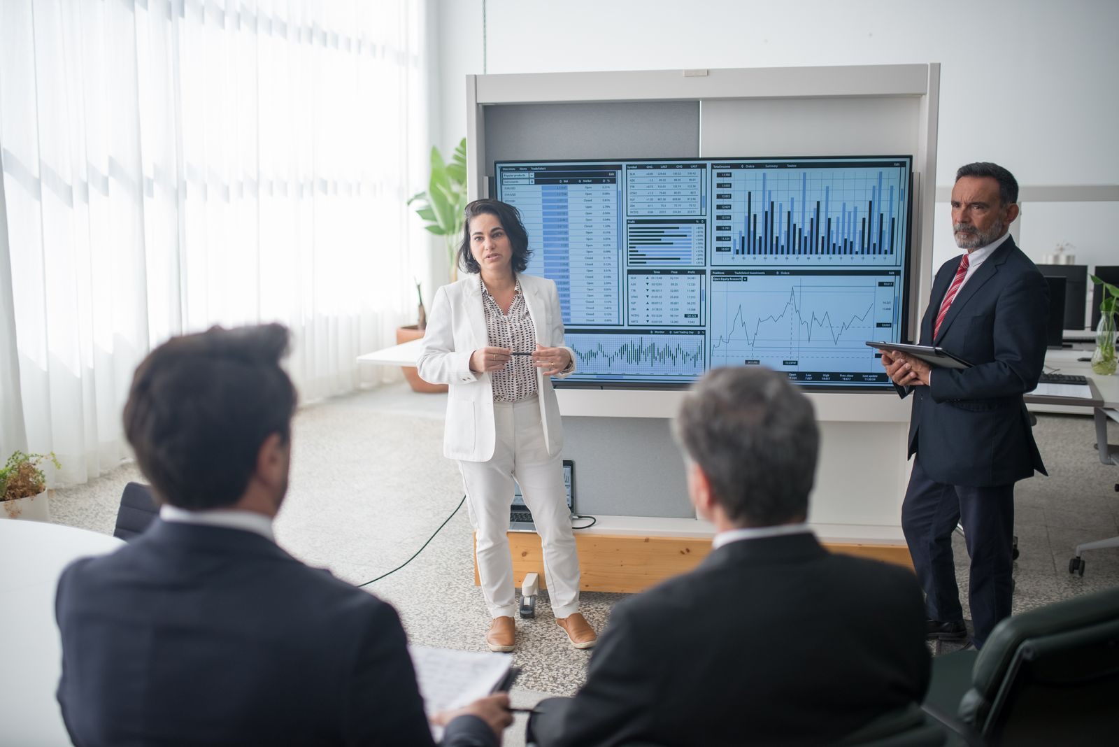 Presenter speaking to a seated group in front of a large screen